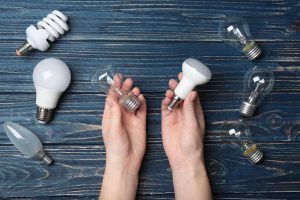 Woman holding LED and incandescent lamp near different light bulbs on wooden background