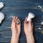 Woman holding LED and incandescent lamp near different light bulbs on wooden background