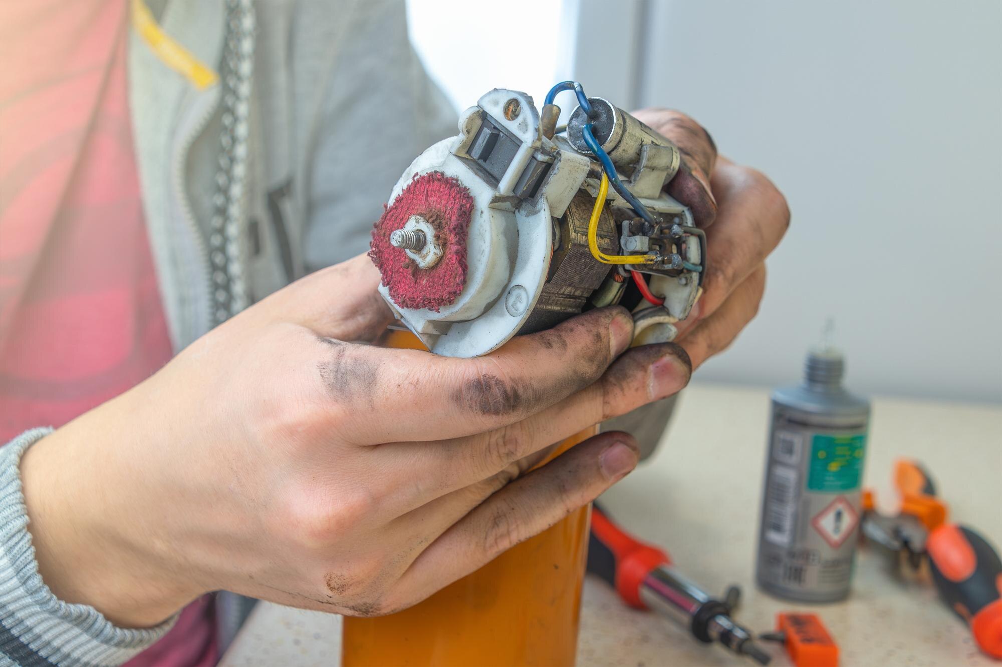 Repair of small household appliances A technician with greasy hands repairs an old coffee grinder examining its small electric motor and wiring
