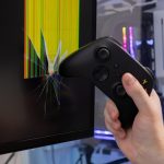 A gamer39s hand holds a black controller near a severely broken computer monitor depicting intense gaming frustration and damaged technology
