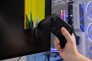 A gamer39s hand holds a black controller near a severely broken computer monitor depicting intense gaming frustration and damaged technology