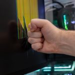 Male clenched fist smashes computer monitor causing shattered screen with colorful pixel lines symbolizing extreme frustration and tech rage