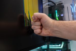Male clenched fist smashes computer monitor causing shattered screen with colorful pixel lines symbolizing extreme frustration and tech rage