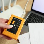 Kobieta trzyma tester prędkości sieci LAN w pobliżu routera Wi-Fi, a użytkownik laptopa sprawdza połączenie internetowe i