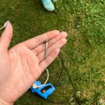 Dziewczyna z niebieskim manicure ma długi gwóźdź w dłoni metalowy gwóźdź srebrny chrom na tle trawy i narzędzi do naprawy budowy domu DIY