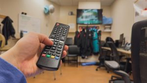 Osoba trzymająca pilota w pokoju z telewizorem w tle.