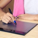 Kobieta w różowy szalik i niebieski manicure rysuje na tablecie przy drewnianym stole z bliska