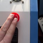 Ręka naciska czerwony przycisk na maszynie