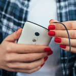 Dziewczyna trzyma mądrze telefon w jej rękach z czerwonym manicure'em w szkockiej kraty koszula i łączy hełmofony