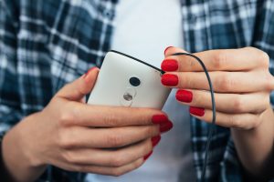 Dziewczyna trzyma mądrze telefon w jej rękach z czerwonym manicure'em w szkockiej kraty koszula i łączy hełmofony