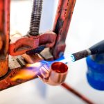 Pracownik przemysłowy używający palnika z propanem do lutowania rur miedzianych