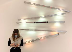 Kobieta w masce stoi przed ścianą z kilkoma światłami.