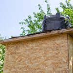 Kabina wiejskiego letniego prysznica z osb z plastikową czarną beczką do podgrzewania wody ze słońca