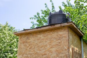 Kabina wiejskiego letniego prysznica z osb z plastikową czarną beczką do podgrzewania wody ze słońca