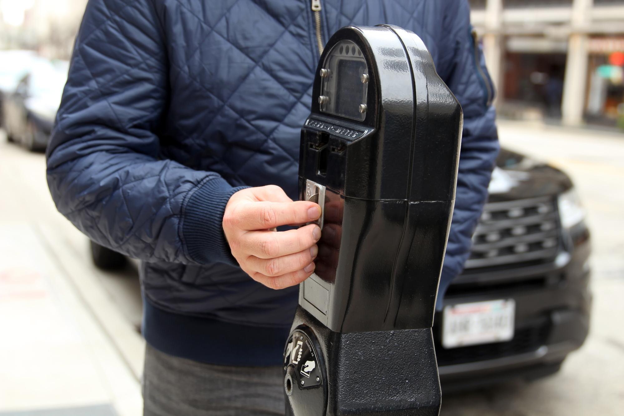 Mężczyzna płaci monetami za parkowanie na nowej ulicy swoim samochodem