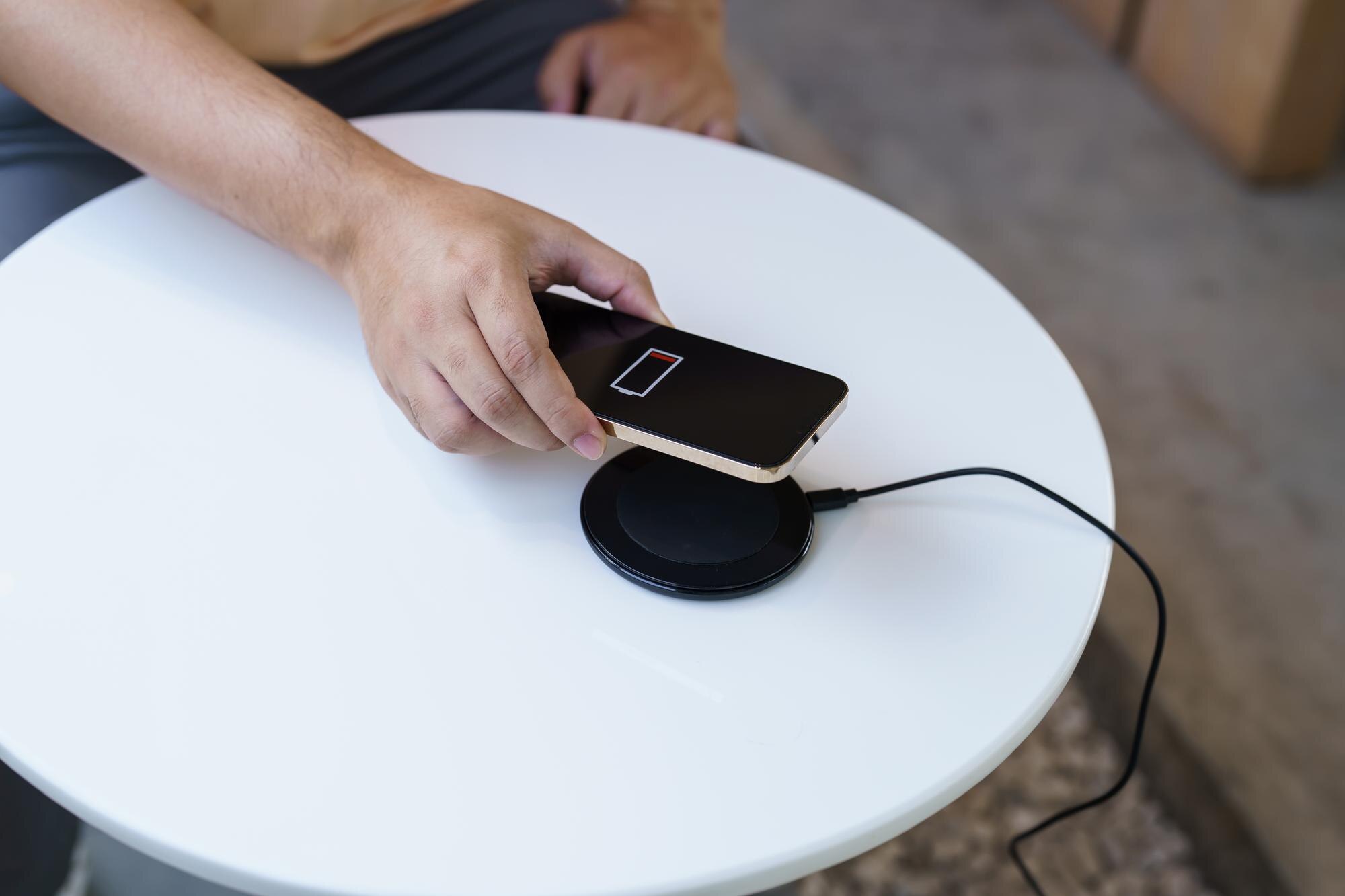 Ładowanie baterii telefonu komórkowego za pomocą bezprzewodowego urządzenia ładującego na stole Ładowanie smartfona na podkładce ładującej Telefon komórkowy w pobliżu ładowarki bezprzewodowej Koncepcja nowoczesnej technologii stylu życia