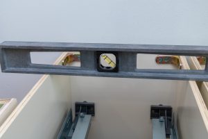 Podczas instalacji nowego zestawu szafek kuchennych pracownik wisi poziomo, aby upewnić się, że szafki są wypoziomowane