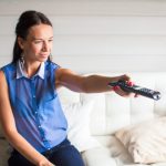 Zamyka w górę portreta kobieta z pilot do tv w jej domu