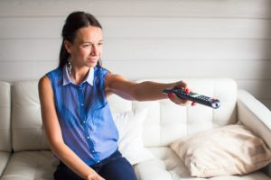 Zamyka w górę portreta kobieta z pilot do tv w jej domu