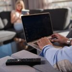 Młoda para relaks w domu przy użyciu tabletów i laptopów, czytając w pobliżu okna na kanapie.