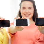 koncepcja technologii i ludzi - uśmiechnięte młode kobiety lub nastolatki pokazujące puste ekrany smartfonów
