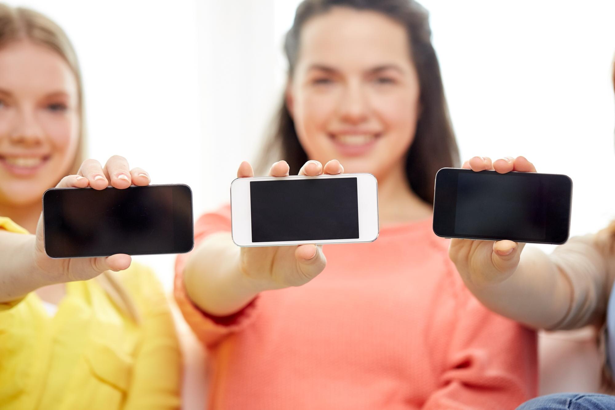 koncepcja technologii i ludzi - uśmiechnięte młode kobiety lub nastolatki pokazujące puste ekrany smartfonów