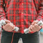 Mężczyzna w czerwonej koszuli z małymi hantlami w rękach