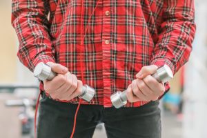 Mężczyzna w czerwonej koszuli z małymi hantlami w rękach