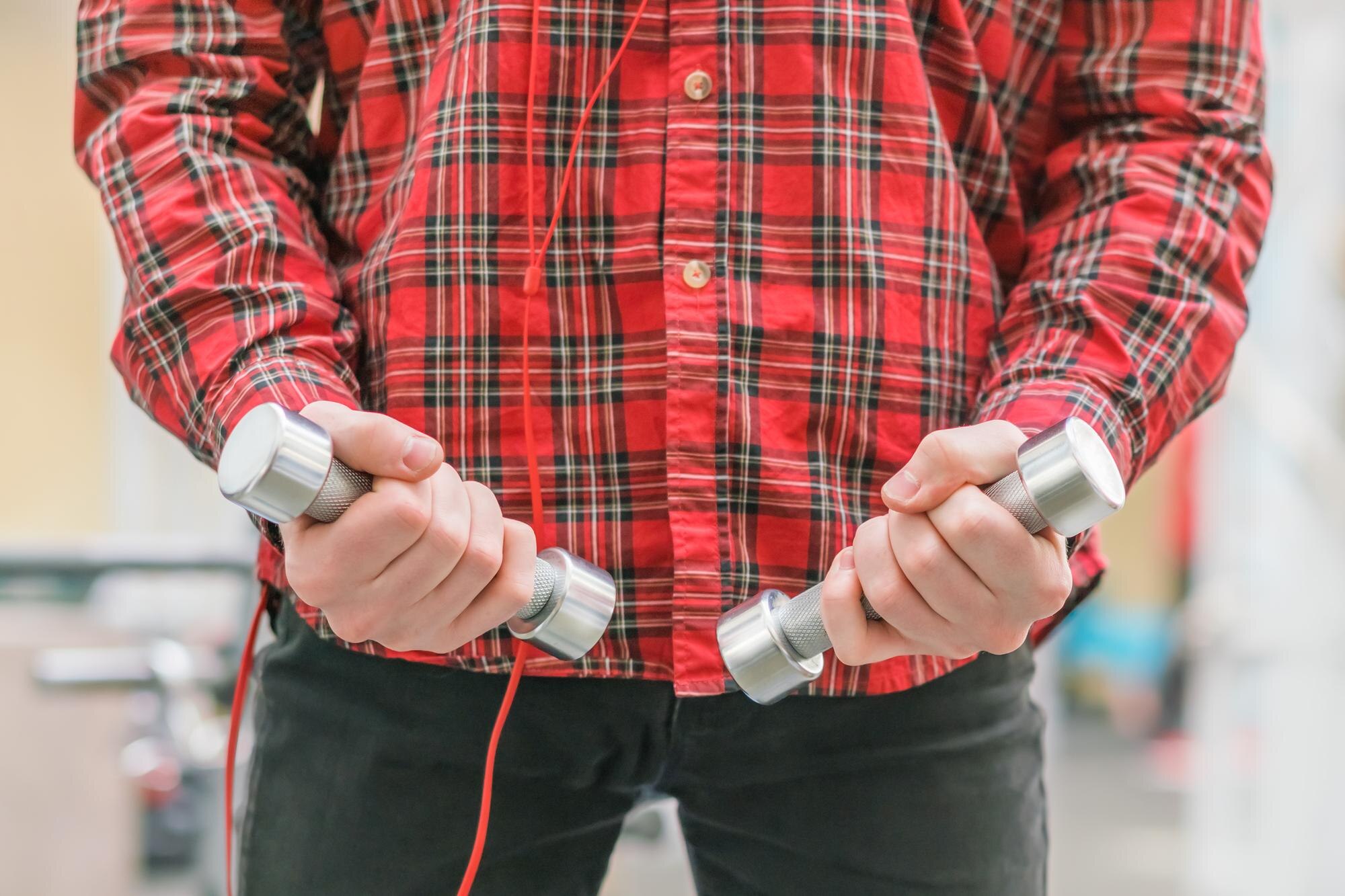 Mężczyzna w czerwonej koszuli z małymi hantlami w rękach