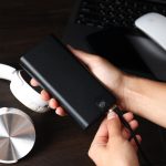 Powerbank w rękach kobiet słuchawki i laptop na ciemnym drewnianym tle