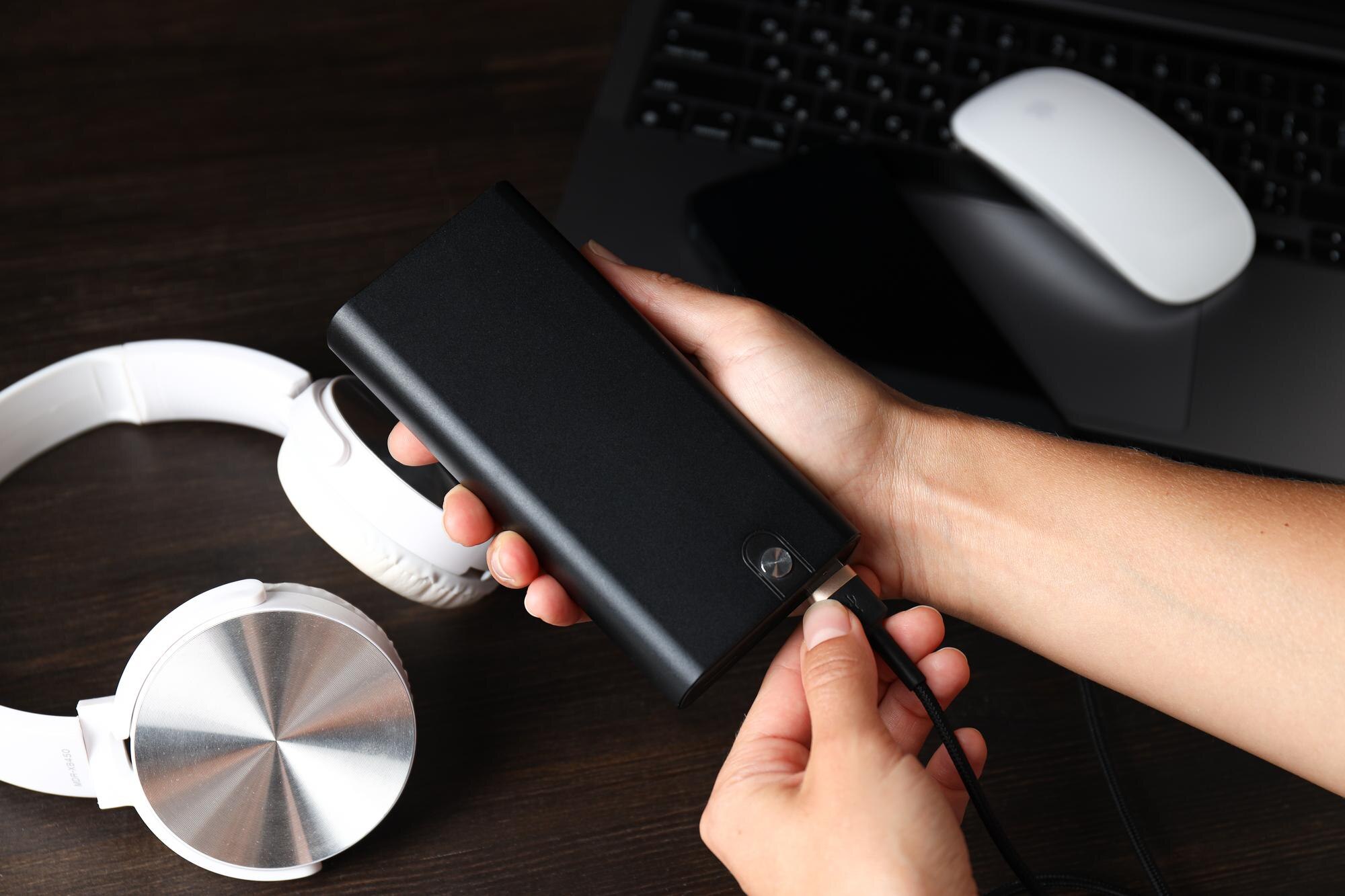 Powerbank w rękach kobiet słuchawki i laptop na ciemnym drewnianym tle