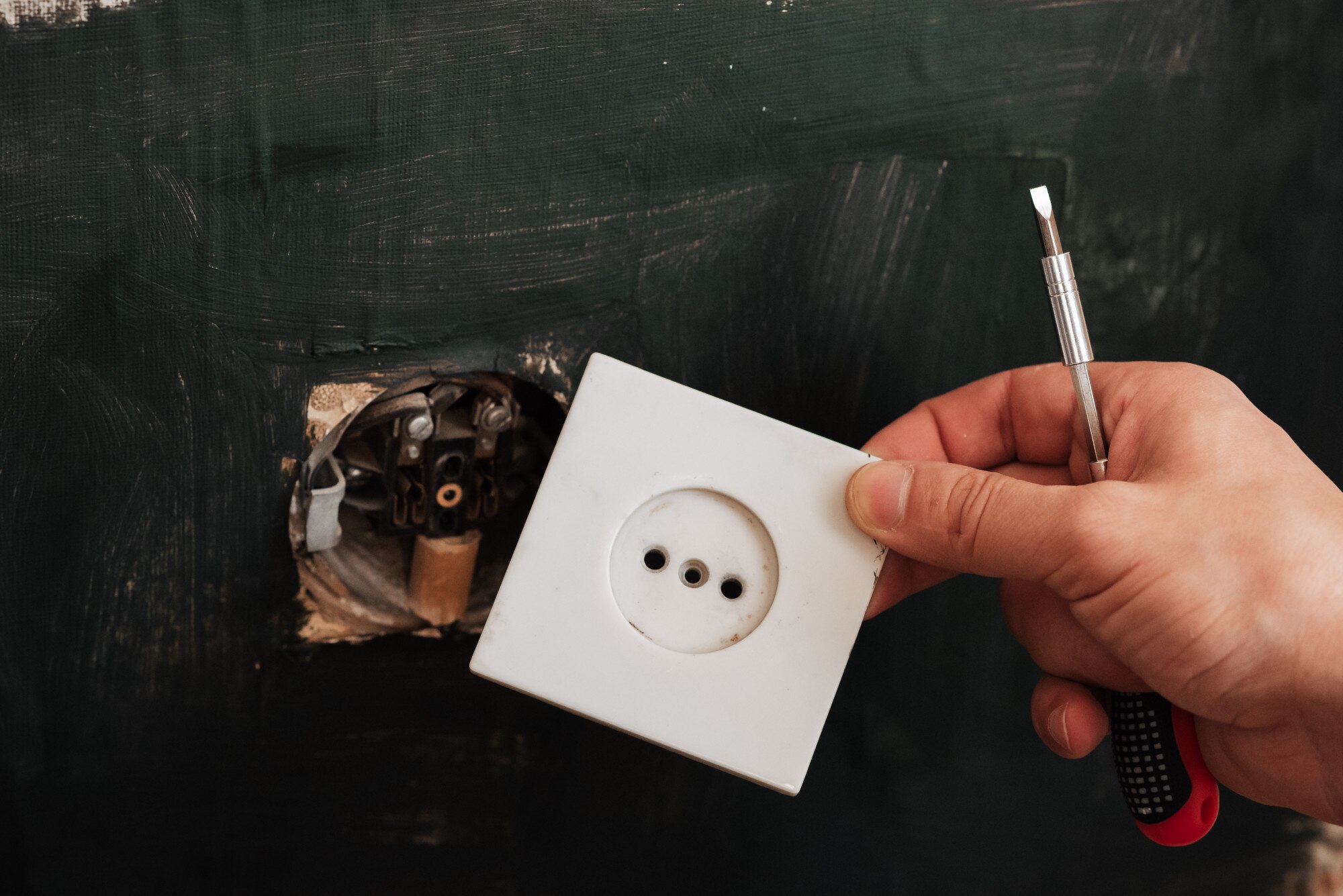 Mężczyzna elektryk usuwa stare gniazdko elektryczne