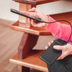 Kobieta ręce trzymając czarny smartfon ładowania baterii z zewnętrznego banku mocy