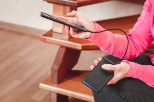 Kobieta ręce trzymając czarny smartfon ładowania baterii z zewnętrznego banku mocy