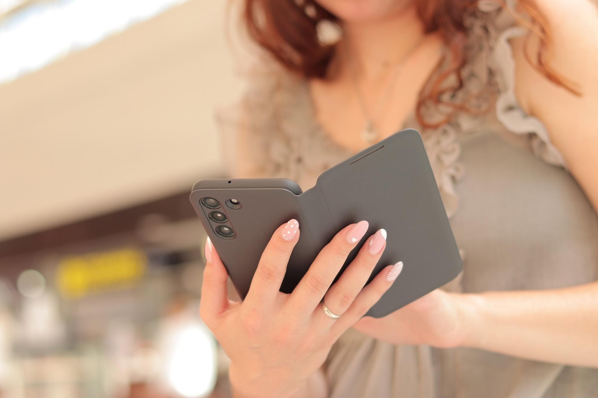 Gadget Girl z telefonem w dłoniach Damskie dłonie ze smartfonem w eleganckim etui z bliska