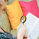 Starsza kobieta rozwiązuje krzyżówki za pomocą szkła powiększającego