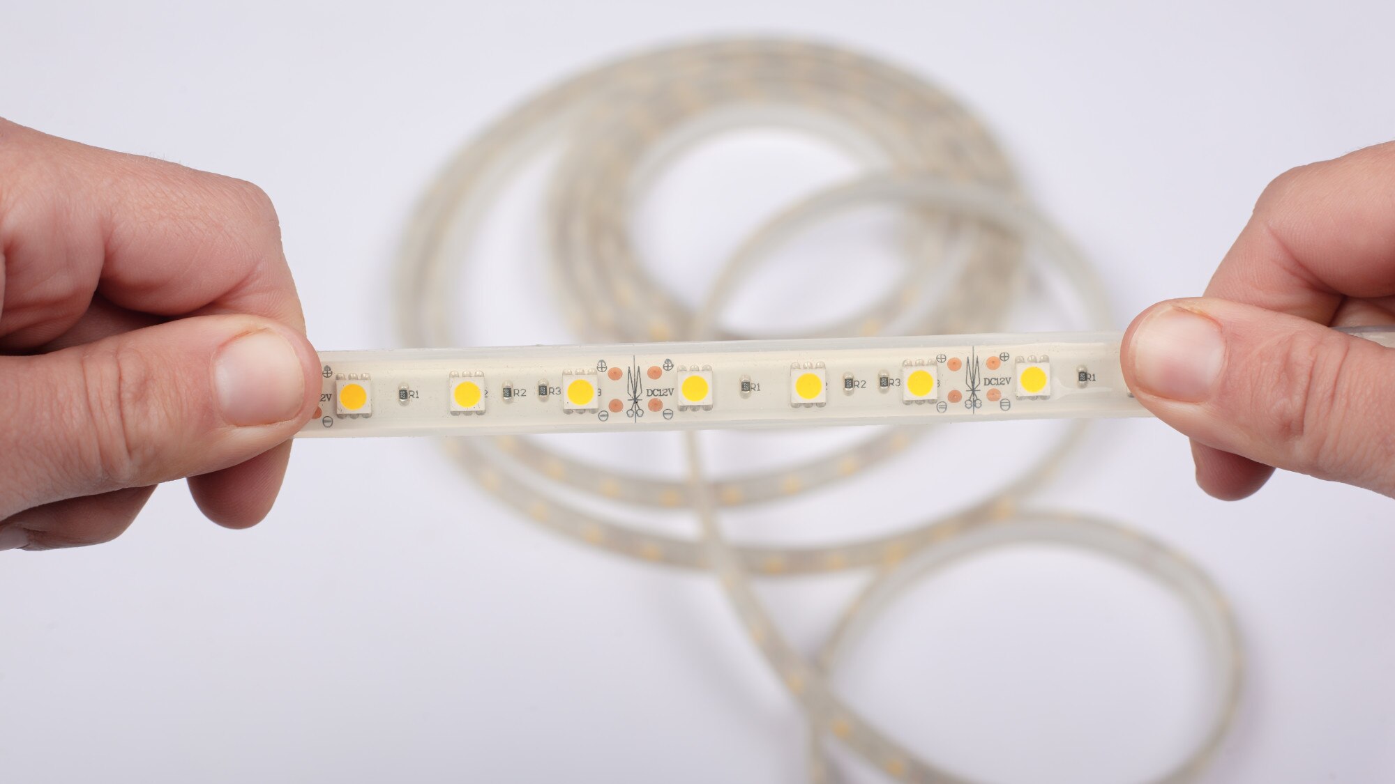 Trzymaj w ręku taśmę LED na białym tle, z bliska.
