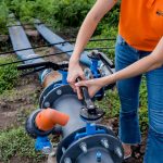 System nawadniania kropelkowego. Energooszczędny system nawadniania kropelkowego stosowany w młodym polu marchwi. Pracownik otwiera kran