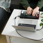 Mężczyzna nagrywa utwór muzyczny elektroniczny za pomocą przenośnej klawiatury midi na laptopie w domowym studiu
