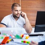 Ojciec z dwoma małymi chłopcami na kolanach próbuje się śmiać w domu. młody człowiek opiekuje się dziećmi i pracuje na komputerze.