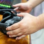 Zbliżony obraz rąk podnoszących okulary VR z oświetloną klawiaturą w tle