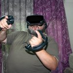 Nadwagi mężczyzna grający w wirtualną rzeczywistość podnoszący ręce z joystickami w VR z fioletowym i szarym tłem