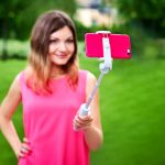 Uśmiechnięta kobieta bierze selfie na telefonie komórkowym z kijem outdoors