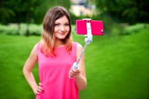 Uśmiechnięta kobieta bierze selfie na telefonie komórkowym z kijem outdoors