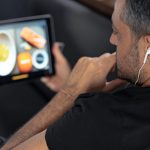 Człowiek za pomocą cyfrowego tabletu i słuchawek, siedząc na kanapie