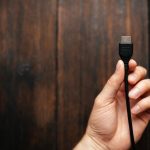 Mężczyzna trzyma w rękach czarny kabel HDMI na ciemnym tle drewnianych