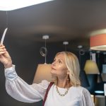 Metka z ceną lampy wiszącej. Kobieta sukcesu z biżuterią na szyi, patrząc na ceną żyrandola, podnosząc rękę, zaciekawiona.