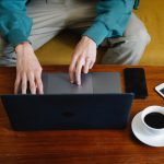 Uśmiechnięty indyjski biznesmen pracujący na laptopie w nowoczesnym biurze