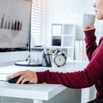 Azjatycka kobieta pracuje z domu w sypialni, korzystając z komputera i pijąc kawę. Przygotowuje dokument finansowy i uczestniczy w internetowym spotkaniu konferencyjnym dotyczącym nowych projektów.